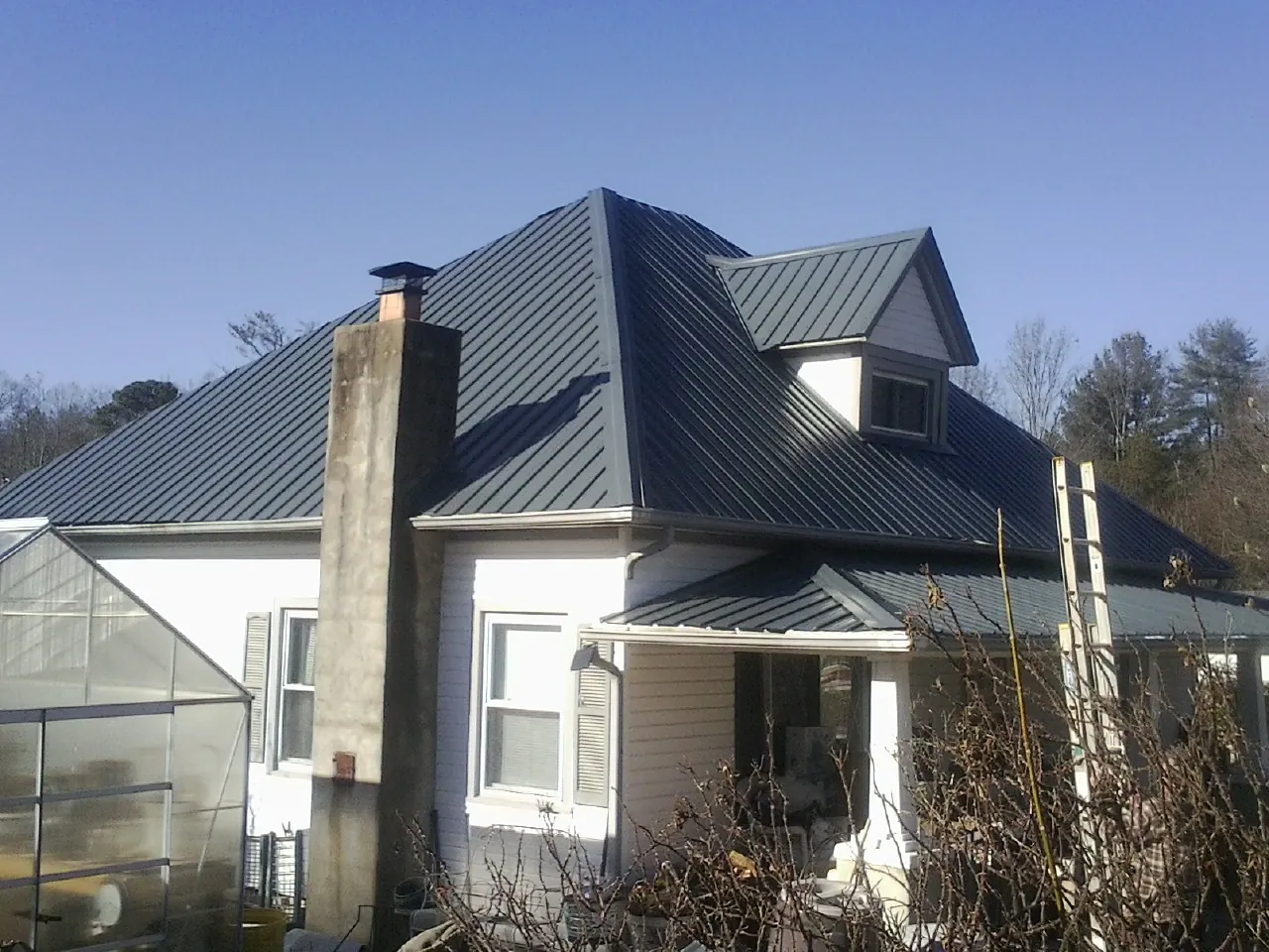 Dark blue standing seam metal roof on a white farmhouse with dormer — Slate & Tile Roof Repair by Roofing Brothers in Mounds