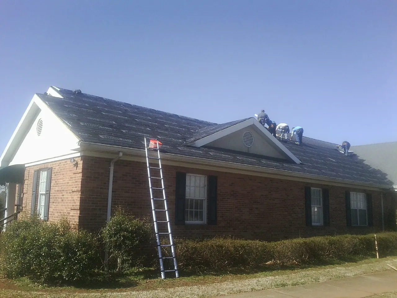 Crew tearing shingles off a brick ranch roof with a ladder set — Metal Roof Repair work by our crew in Mounds
