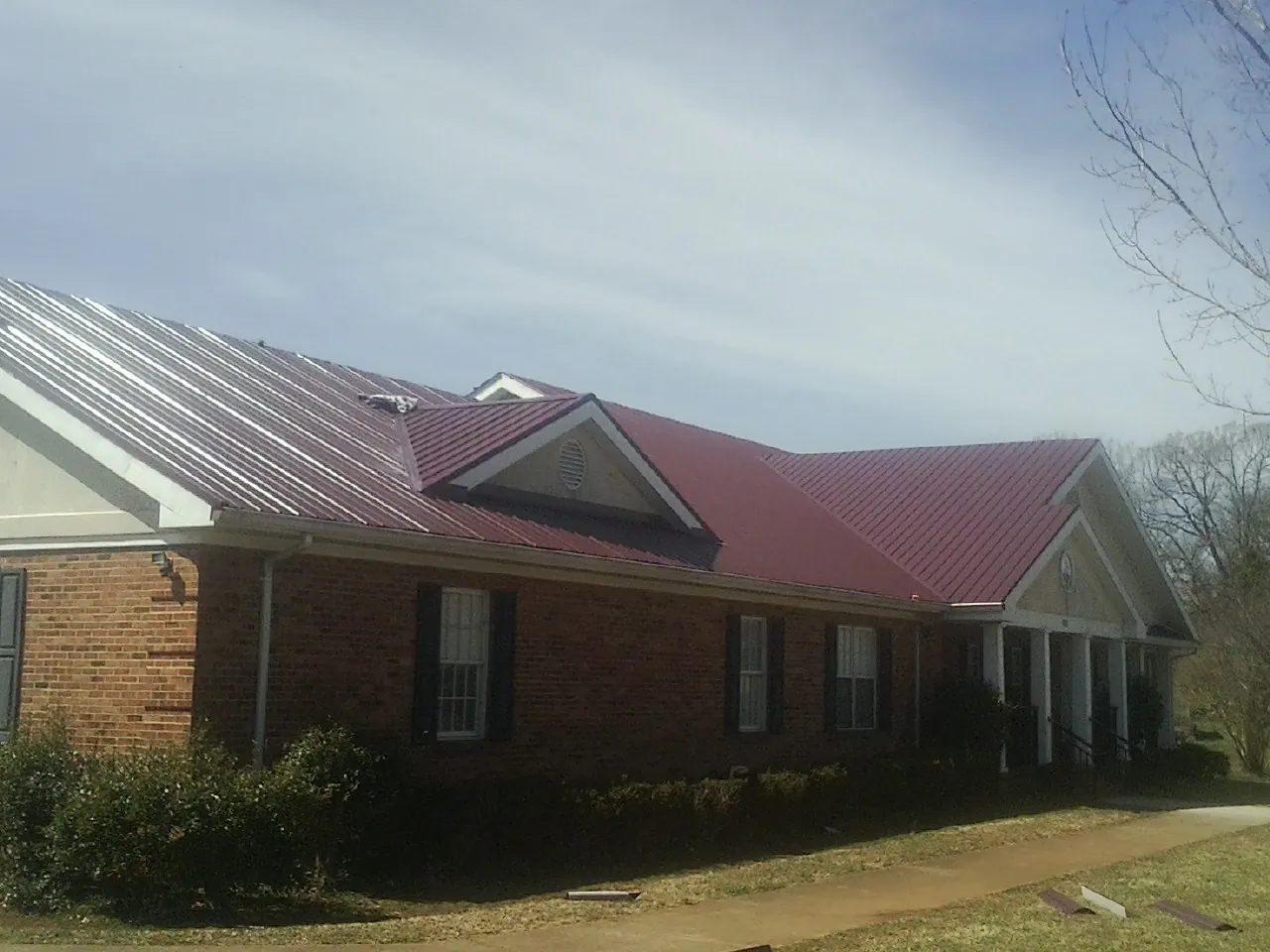 Red metal roof with gabled entries on a long brick building, from a Hail Damage Roof Repair job in Mounds