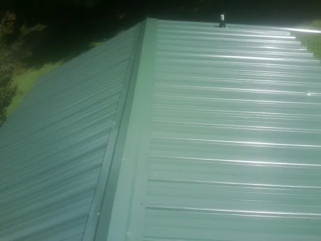 New green metal panels meeting at the ridge of a roof — Flat Roof Repair work by our crew in Mounds