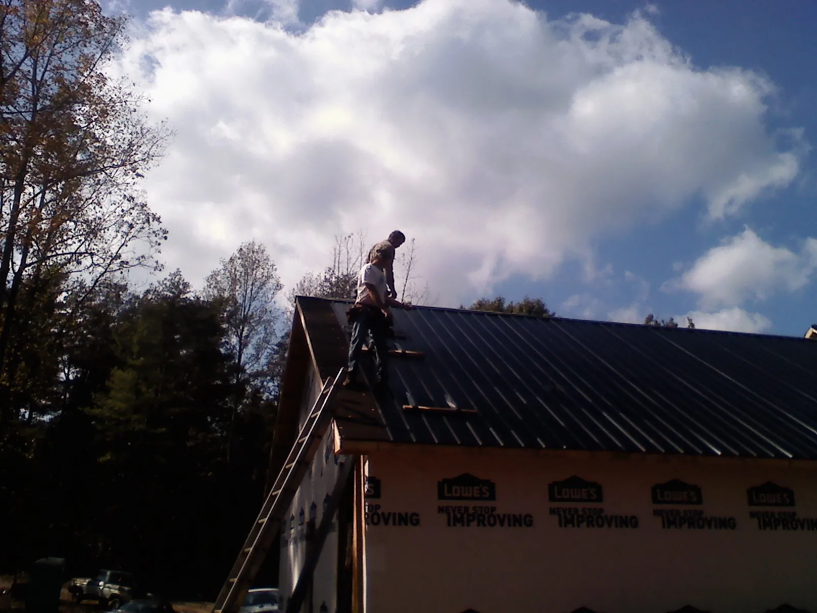 Roofer fastening dark metal panels high against a cloudy sky, from a Roof Inspection job in Mounds
