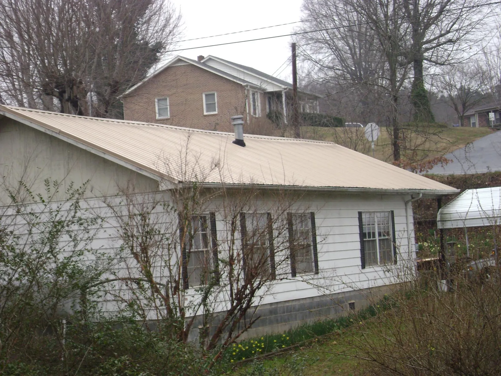 Tan metal roof on a white sided house set into a hillside — Commercial Roofing by Roofing Brothers in Mounds